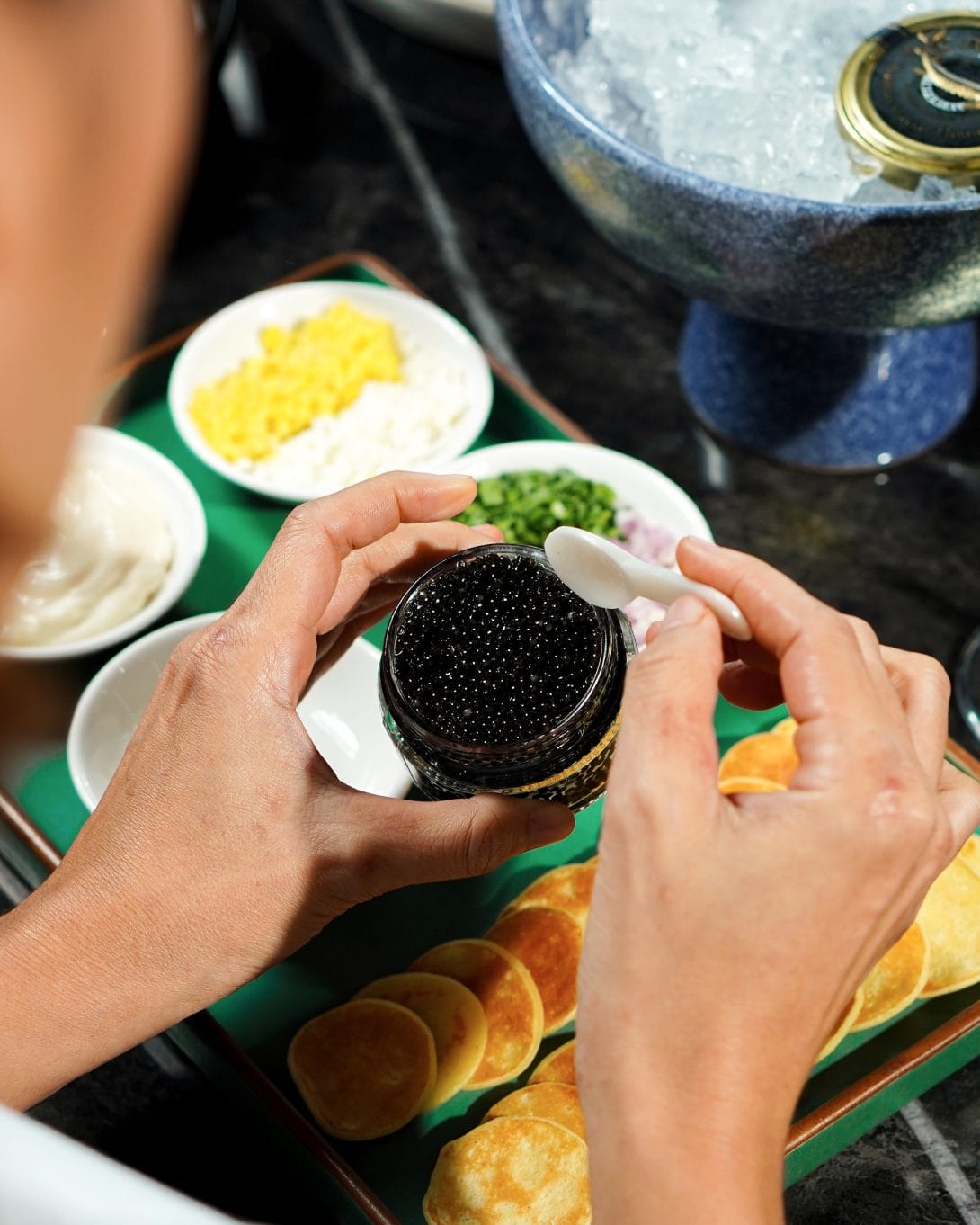 A person holding a container of cavier with condiments in the background