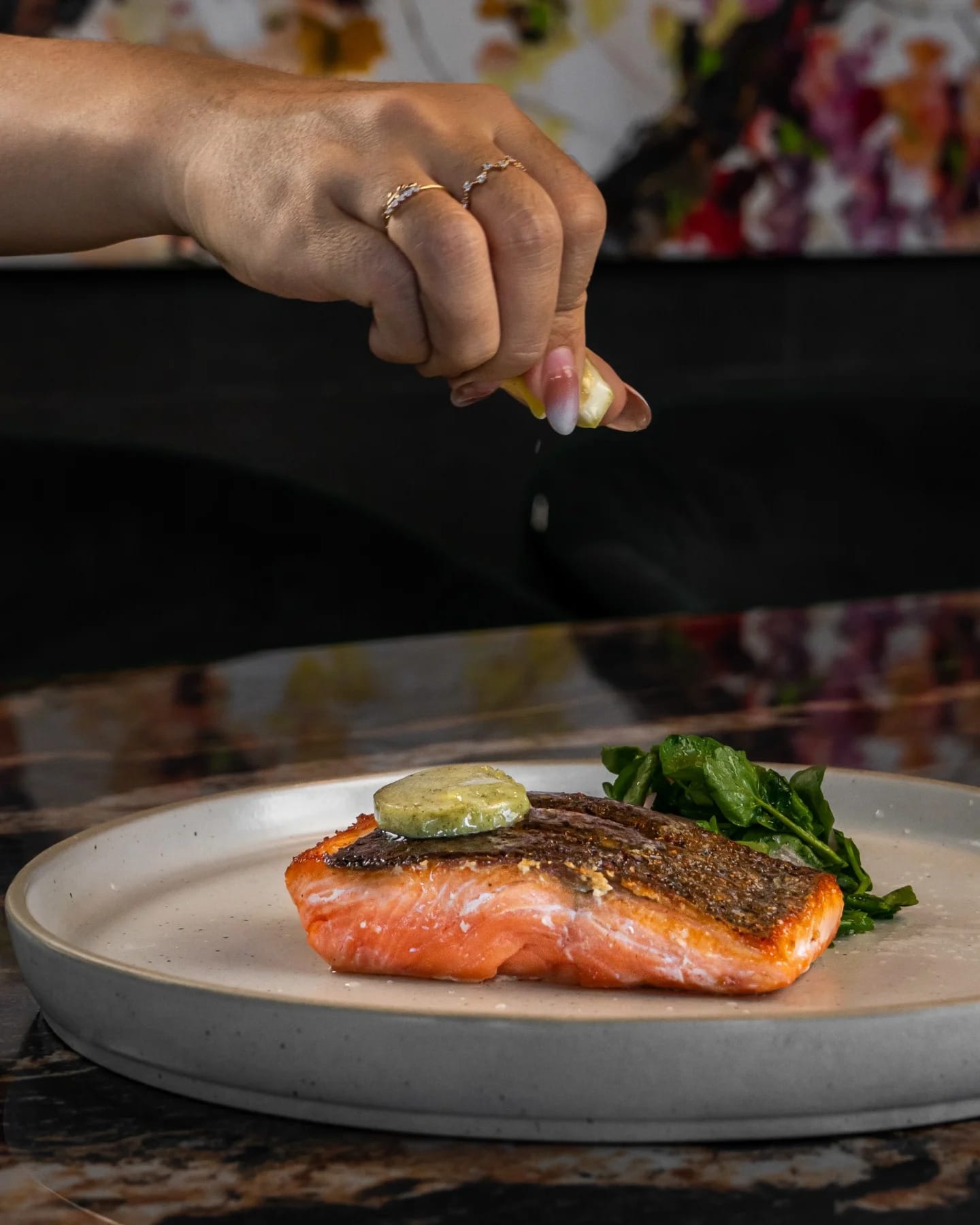 A catering chef in Canggu squeezing lemon to a finished plate of salmon with salad garnish